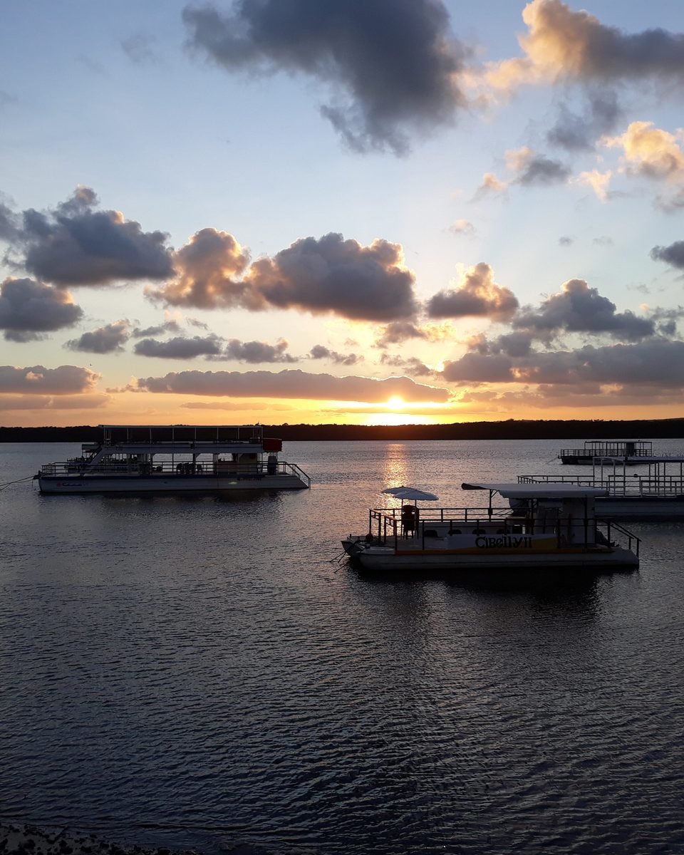 Pôr do sol sobre o rio Paraíba na Praia do Jacaré, em Cabedelo, com barcos-bar ancorados e o reflexo do sol na água