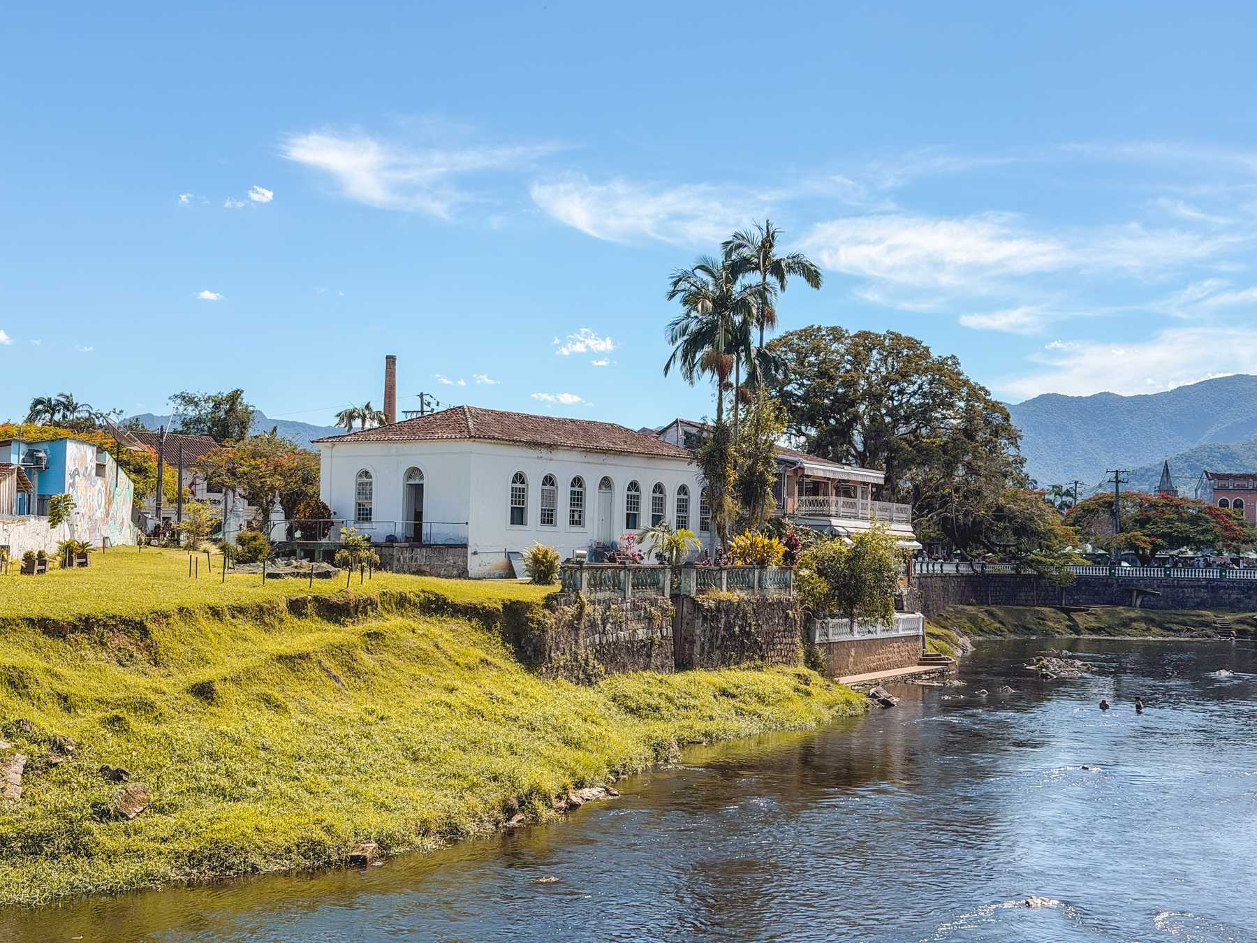 Rio Nhundiaquara passando pelo centro histórico de Morretes, com casarão branco, palmeiras e a Serra do Mar ao fundo.