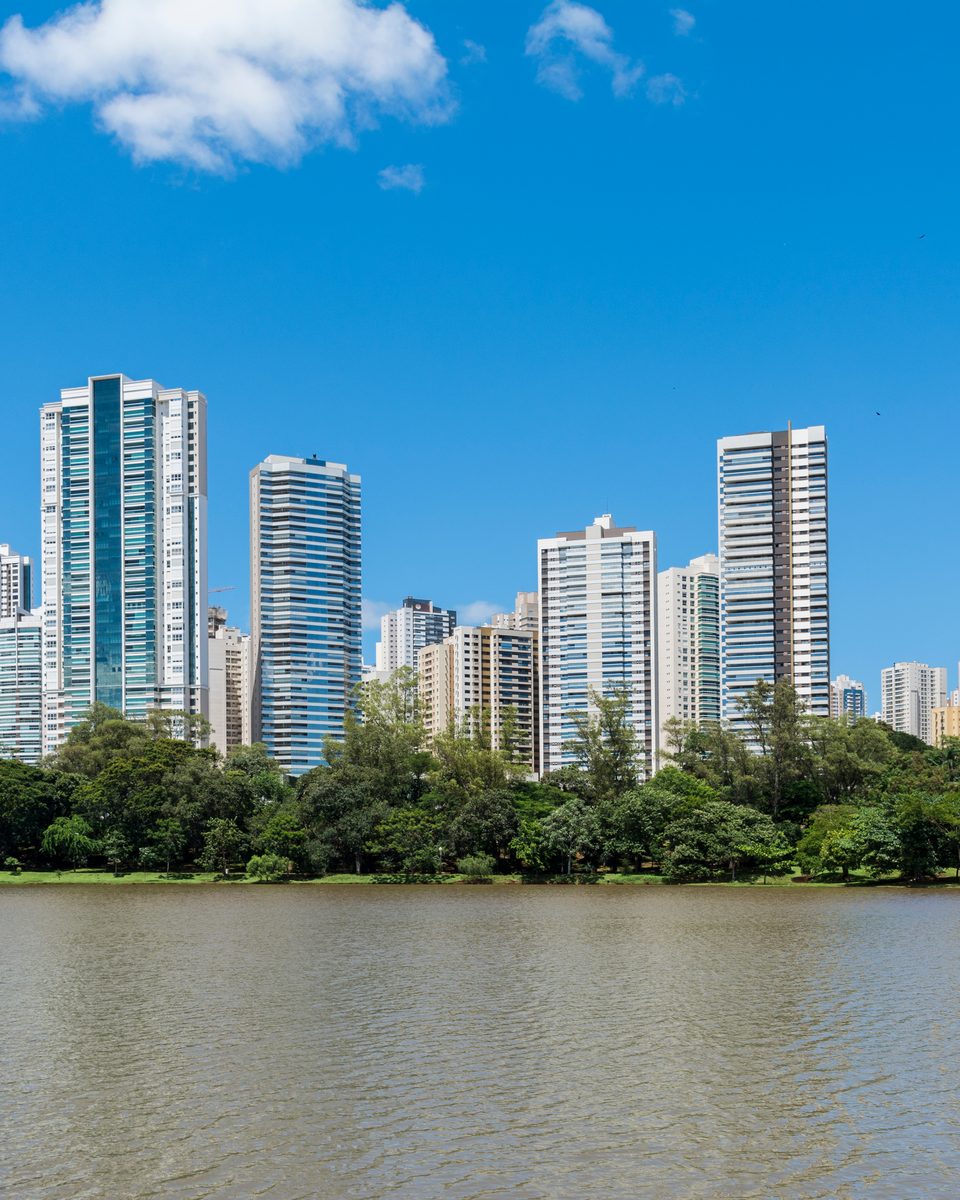 Prédios residenciais de Londrina às margens do Lago Igapó, com a mata na beira da água e o céu azul com nuvens.