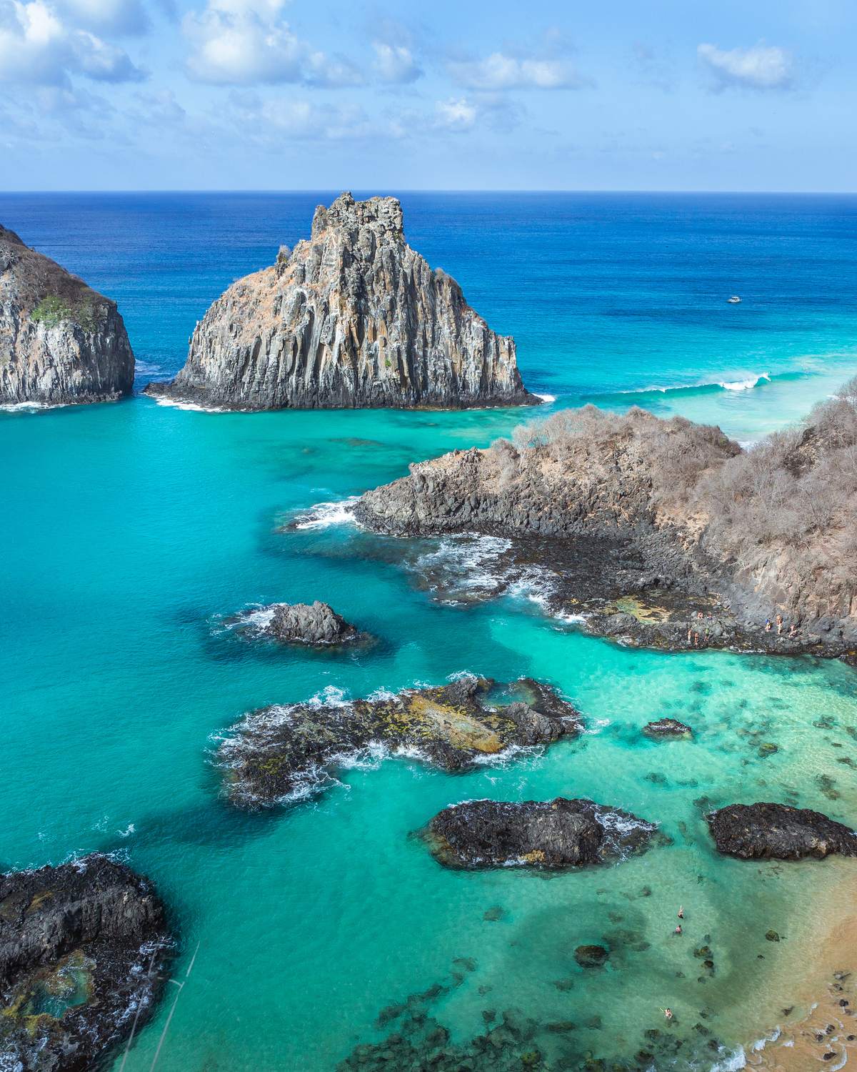 Morro Dois Irmãos, dois morros de pedra lado a lado no mar azul-turquesa de Fernando de Noronha, vistos do alto com as rochas e a faixa de areia em primeiro plano.