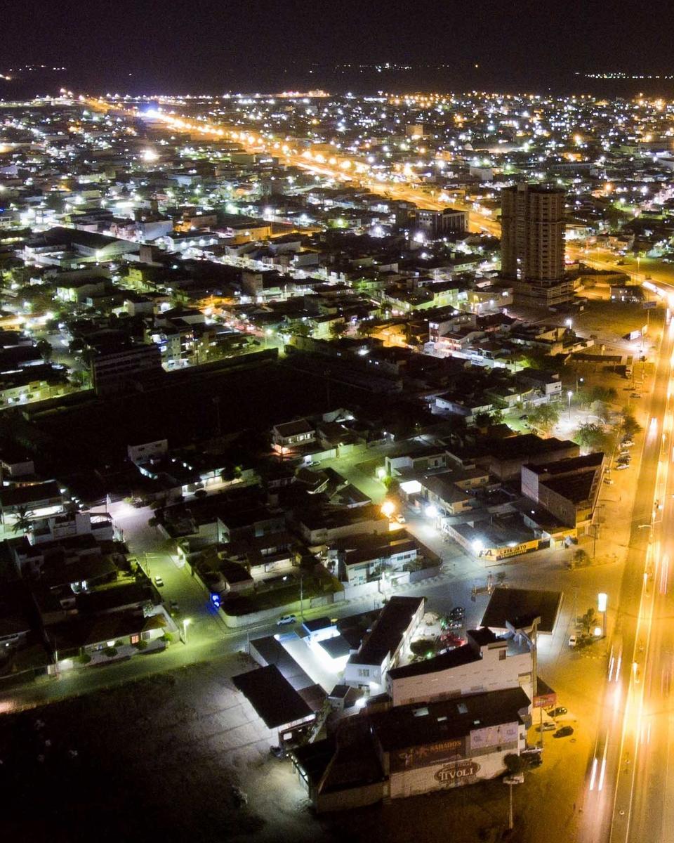 Vista noturna do alto de Santa Cruz do Capibaribe, com a avenida principal iluminada cortando a cidade, prédios e o casario aceso até o horizonte.