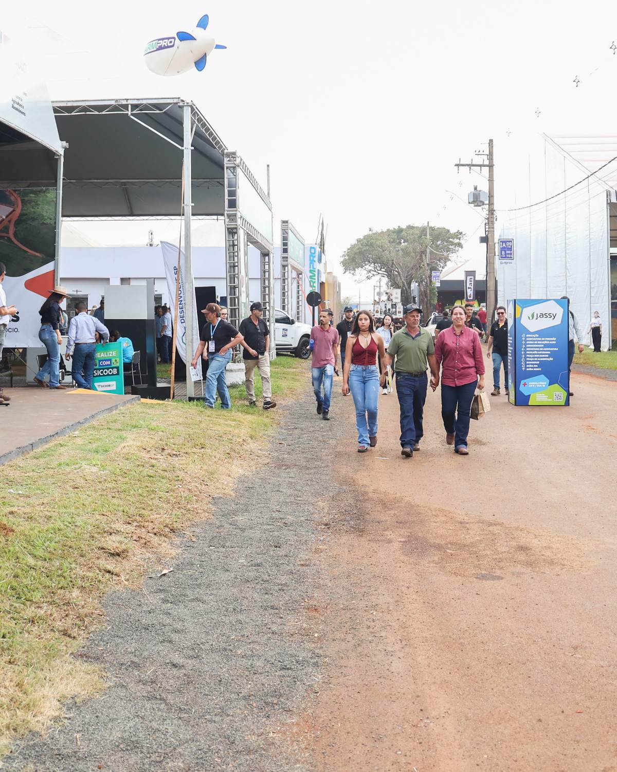 Rapaz de boné e camiseta preta segurando o celular enquanto caminha por uma rua de terra entre os estandes da Agrishow, em Ribeirão Preto.
