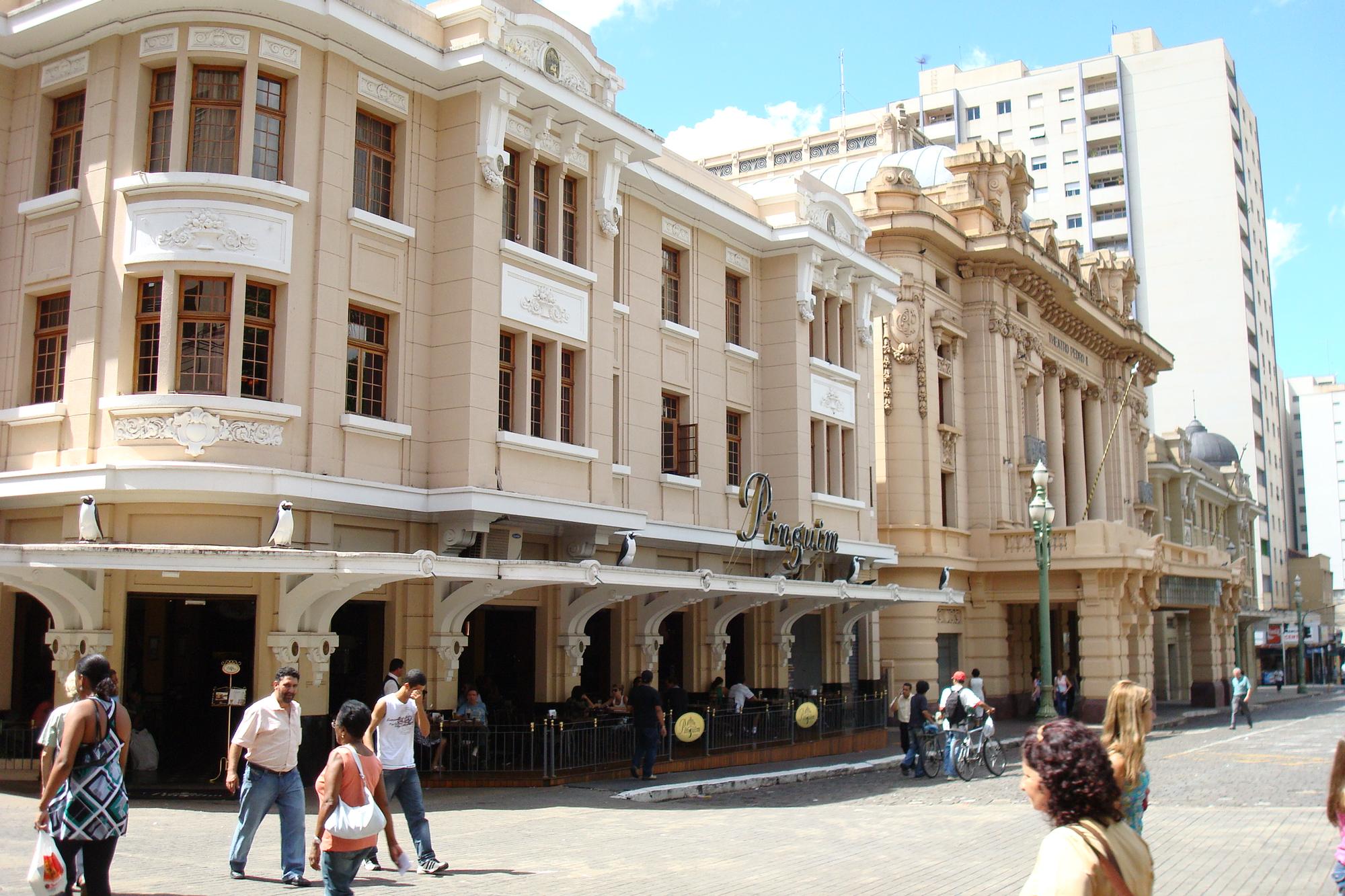 Pessoas caminhando no calçadão do Quarteirão Paulista, em Ribeirão Preto, em frente ao prédio histórico da Choperia Pinguim e ao Theatro Pedro II, num dia de sol.