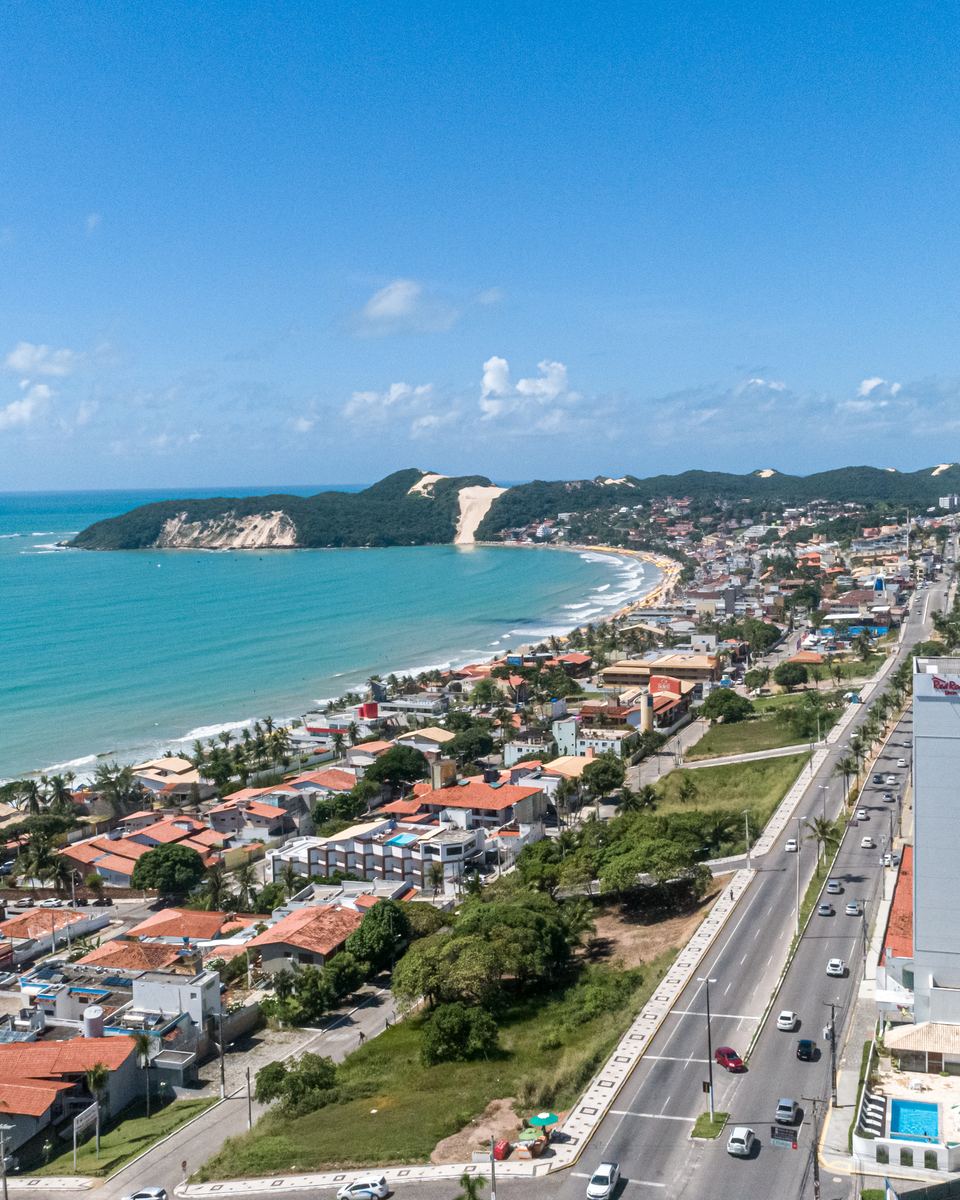 Banhistas na areia e na beira d'água da praia de Ponta Negra, em Natal, com os prédios da orla ao fundo