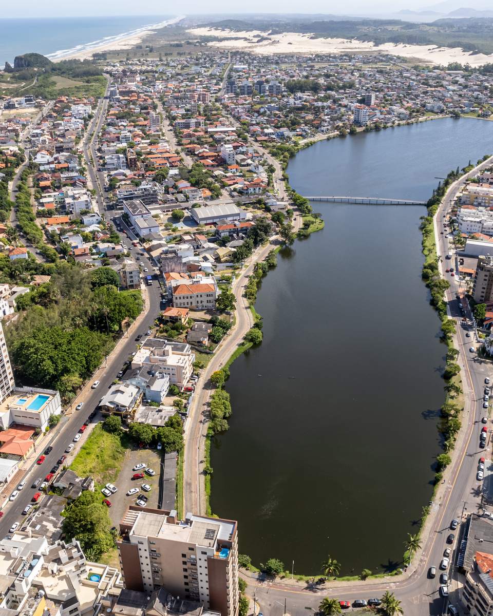 Vista aérea de Torres, com prédios perto do mar, uma lagoa atravessando a cidade, os morros da costa e o oceano ao fundo.