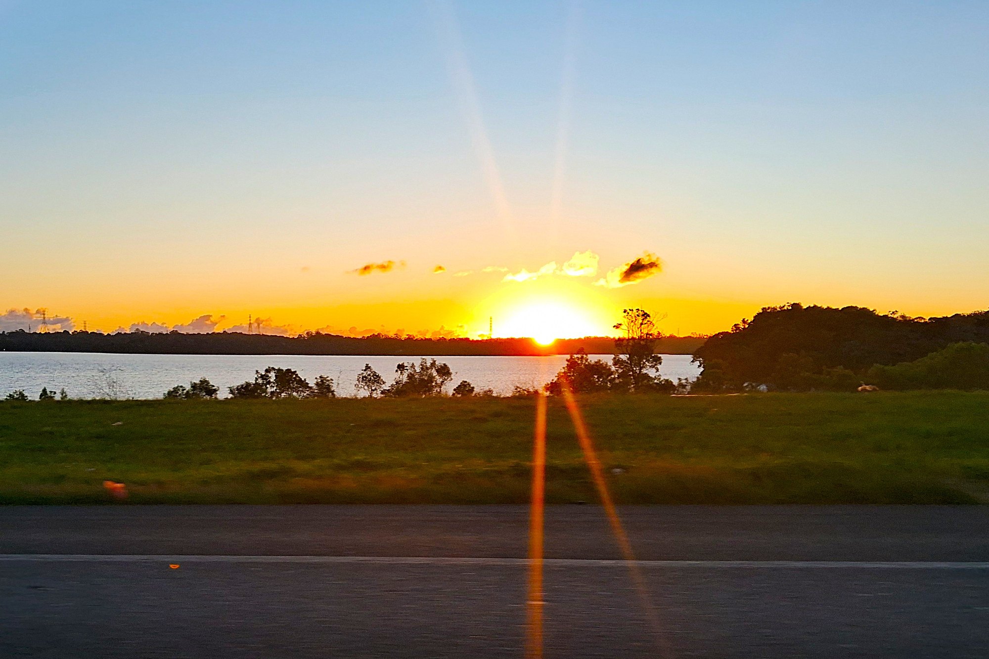 Pôr do sol sobre a Represa Billings, em São Bernardo do Campo, com a margem de mata, o gramado e a pista em primeiro plano.