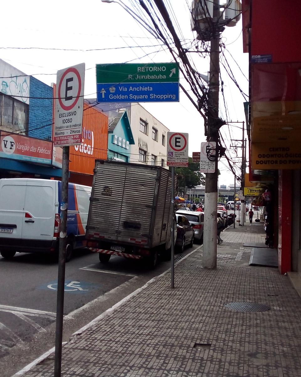 Calçada da Rua Marechal Deodoro, no Centro de São Bernardo do Campo, com lojas, um motociclista e placas indicando a Rua Jurubatuba e a Via Anchieta.