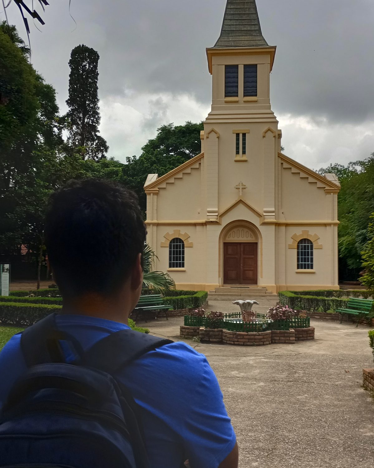 Rapaz de mochila, de costas, olhando a capela amarela do Parque Vicentina Aranha, em São José dos Campos.