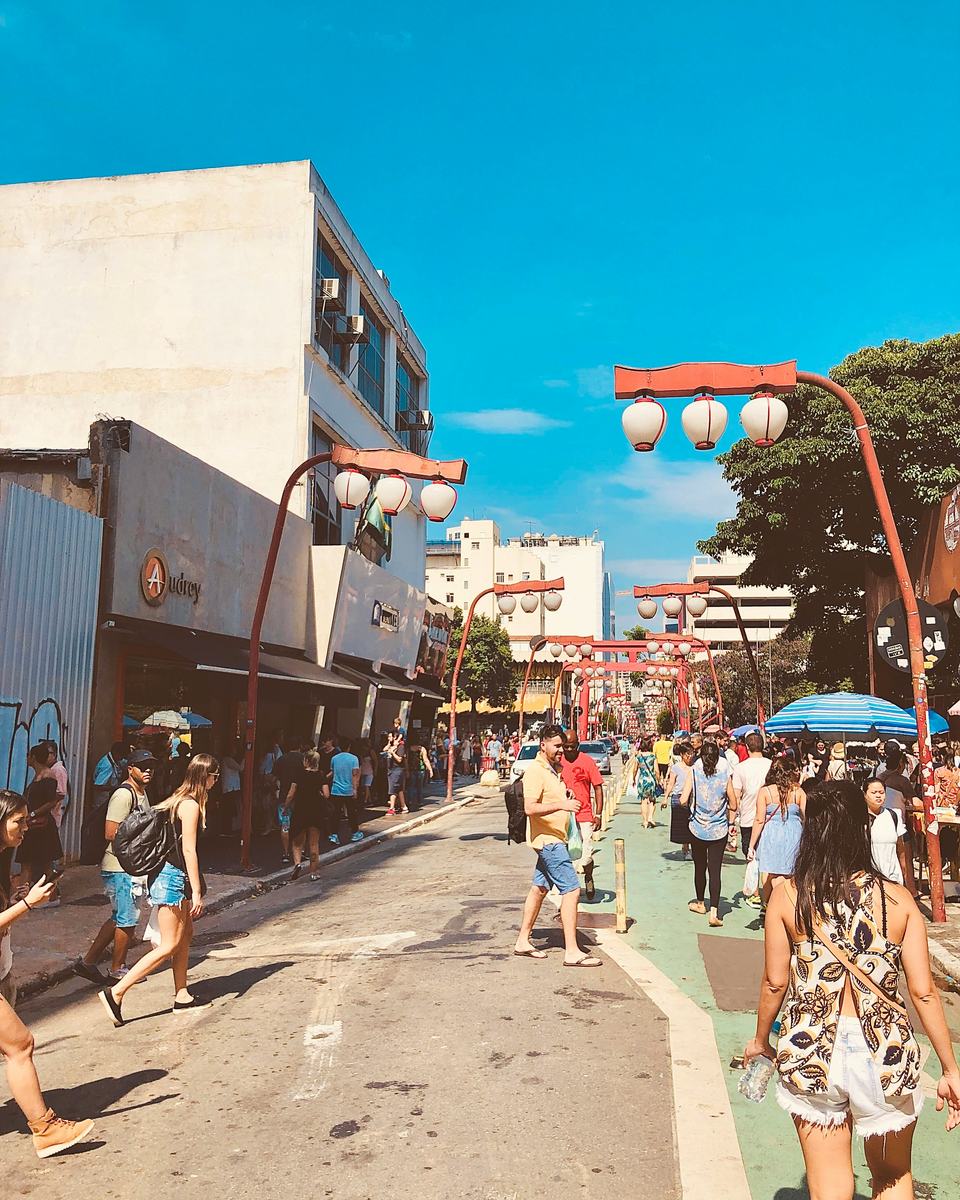 Rua do bairro da Liberdade, em São Paulo, com lojas, pedestres e as luminárias vermelhas.