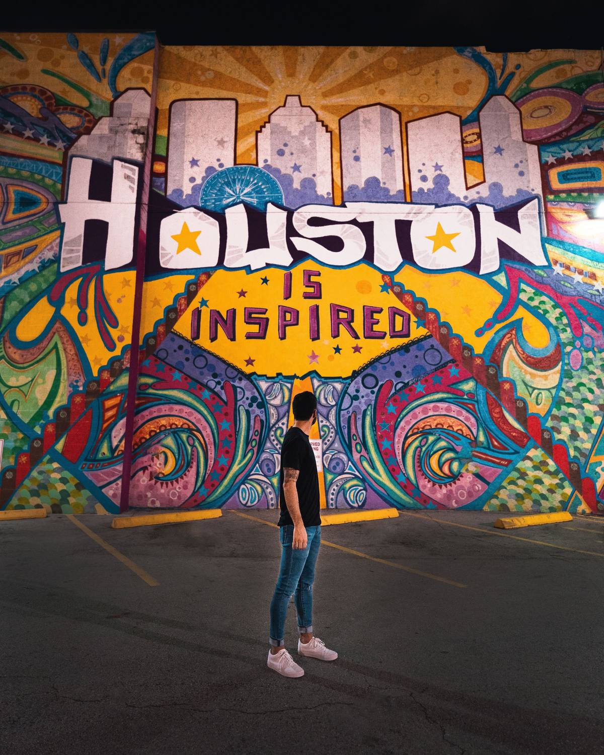 Homem de costas diante do mural colorido Houston Is Inspired, iluminado à noite, em Houston.