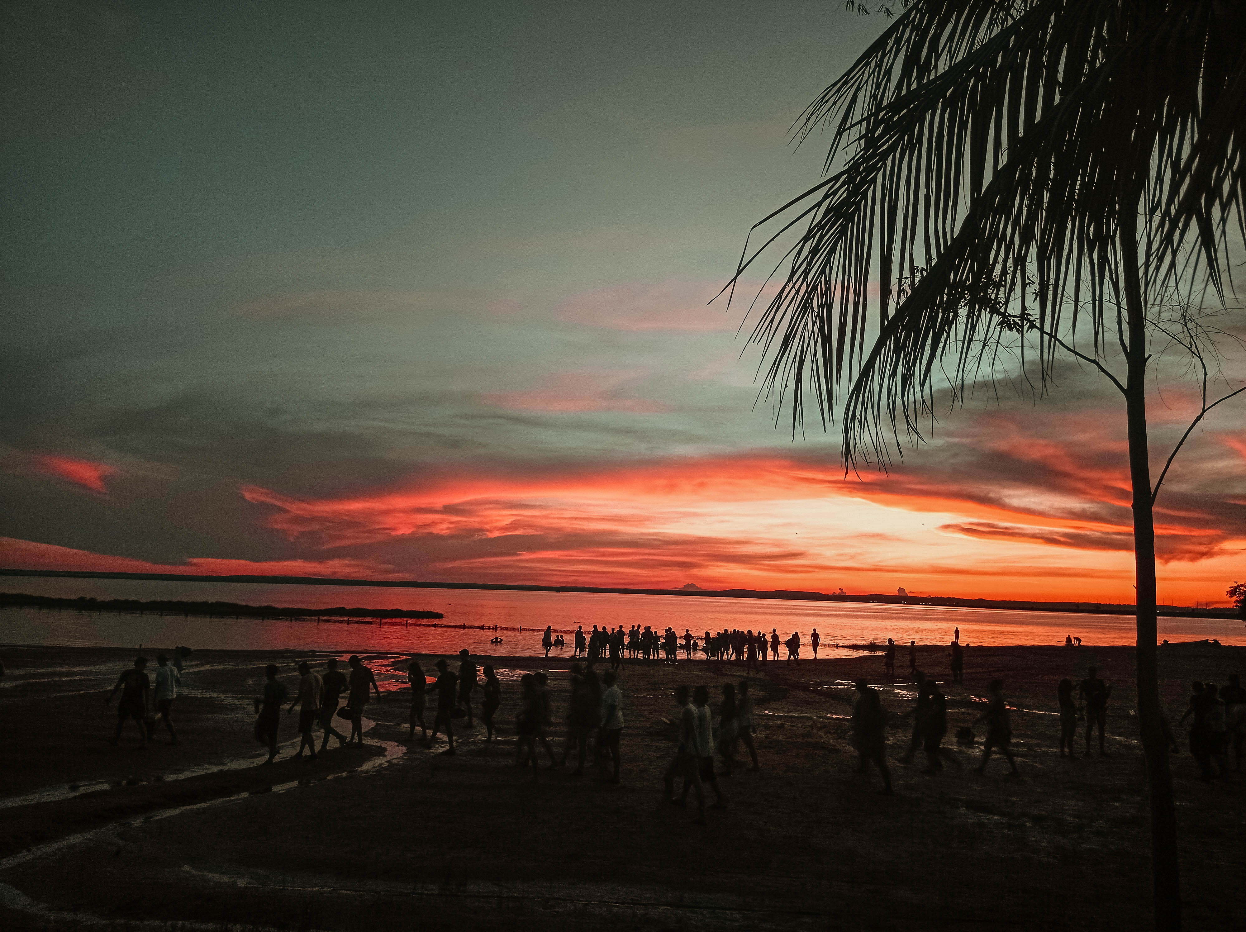 Pôr do sol na Praia da Graciosa, em Palmas, com o céu em tons de laranja e rosa refletido no Rio Tocantins e pessoas na faixa de areia