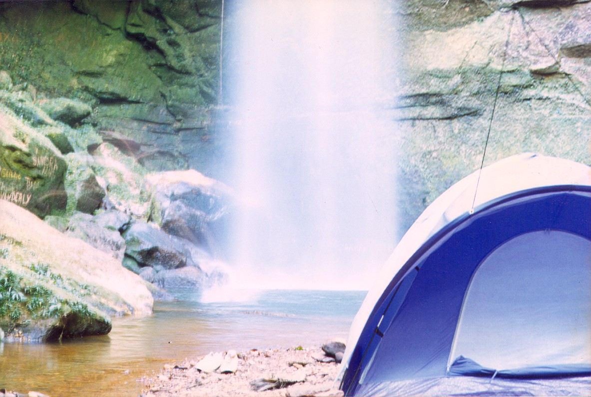 Cachoeira caindo entre rochas cobertas de vegetação em Taquaruçu, distrito de Palmas, com barraca de acampamento no primeiro plano