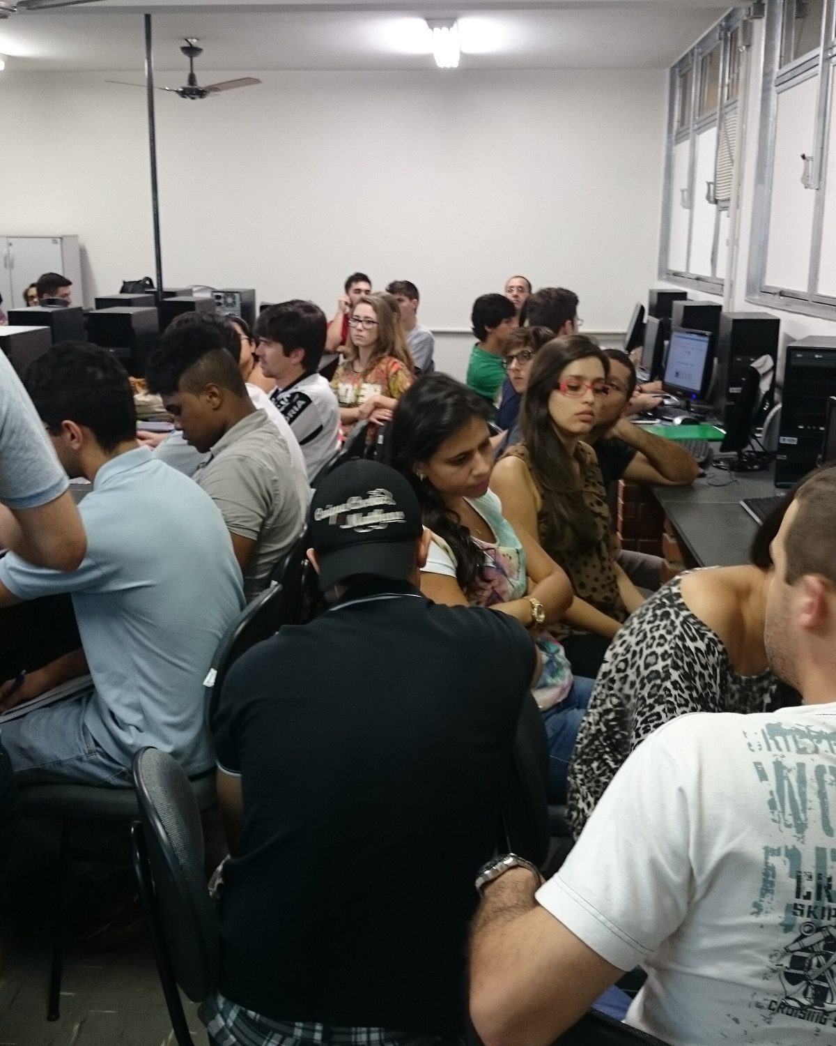 Estudantes sentados em fileiras diante de computadores numa sala de aula da Universidade Federal de Uberlândia, conversando e acompanhando uma oficina.