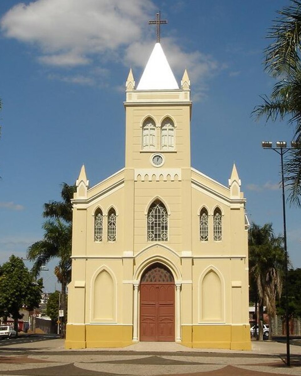 Fachada amarela e branca da Igreja de Nossa Senhora do Rosário, em Uberlândia, com torre pontuda e porta vermelha, entre palmeiras, na praça onde termina a Festa da Congada.