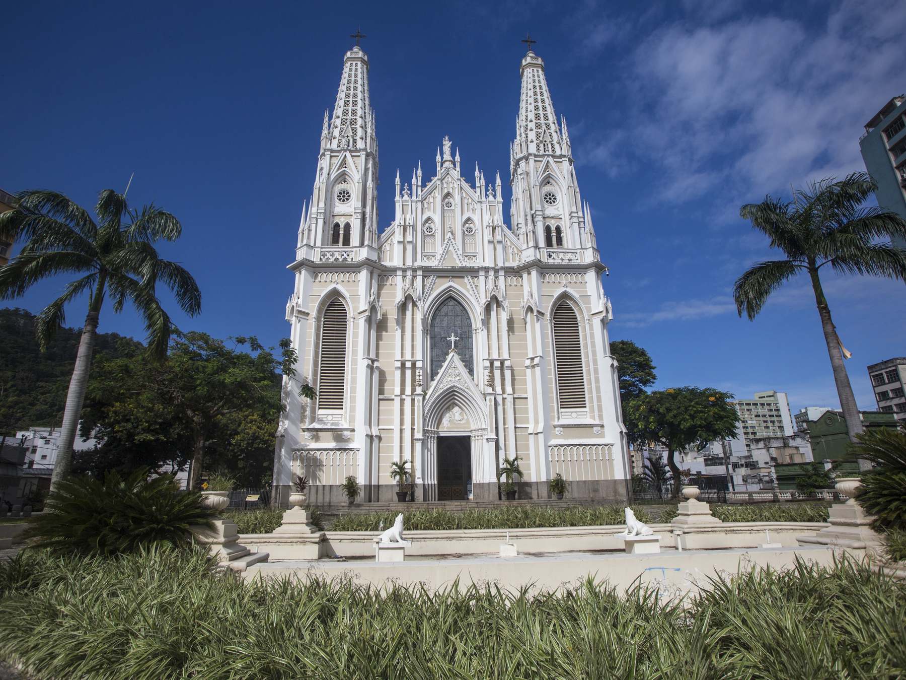 Catedral Metropolitana de Vitória, em pedra clara e estilo neogótico, com as duas torres apontadas para o céu azul e palmeiras dos dois lados.