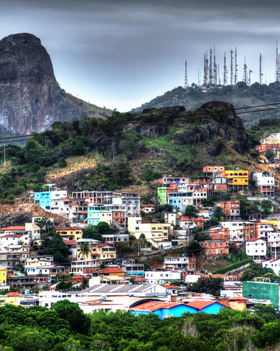 Pedra dos Olhos erguida sobre a encosta verde do Parque Estadual da Fonte Grande, com casas coloridas espalhadas pelo morro abaixo dela.