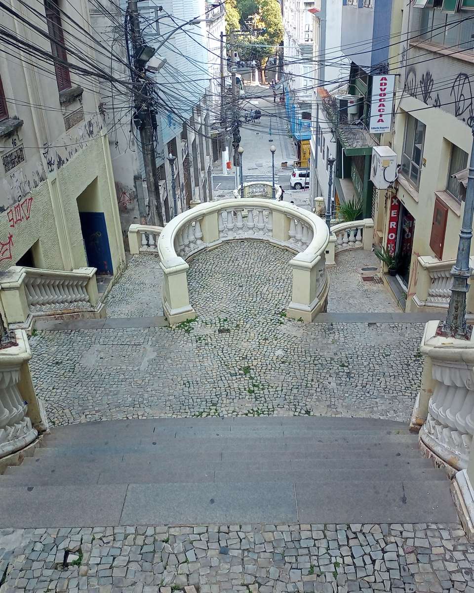 Escadaria Maria Ortiz vista do alto, com os degraus e o piso de pedra portuguesa descendo entre os casarões do Centro de Vitória até a rua movimentada lá embaixo.